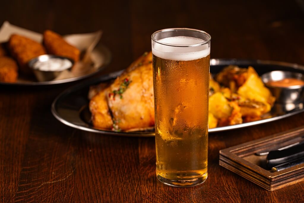 Čaša svetlog lager piva uz poslužen obrok na drvenom stolu u restoranu