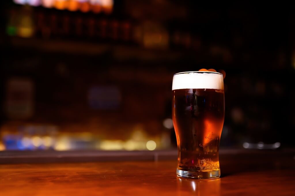 Čaša piva sa bogatom penom servirana na šanku u ambijentu bara
